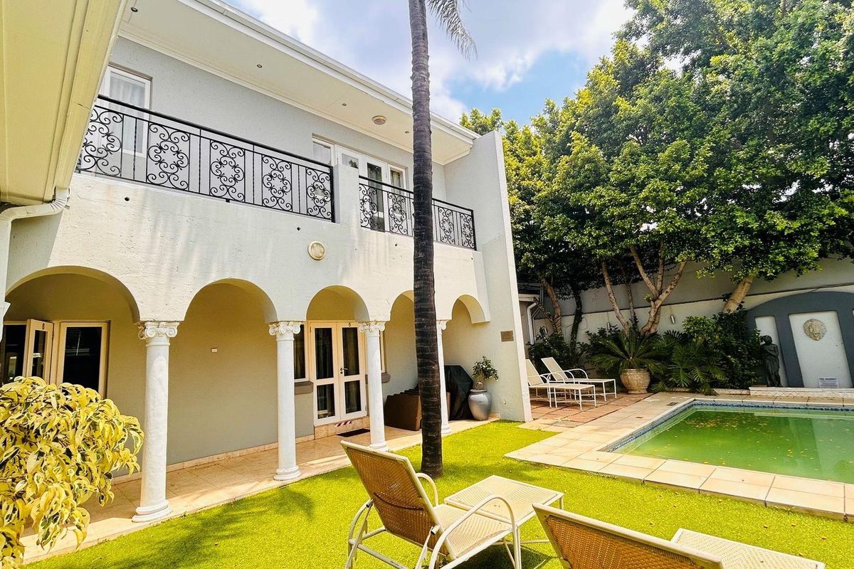 Rear exterior view featuring a covered patio with arched columns, a balcony with wrought iron railings, a swimming pool, and landscaped garden area.