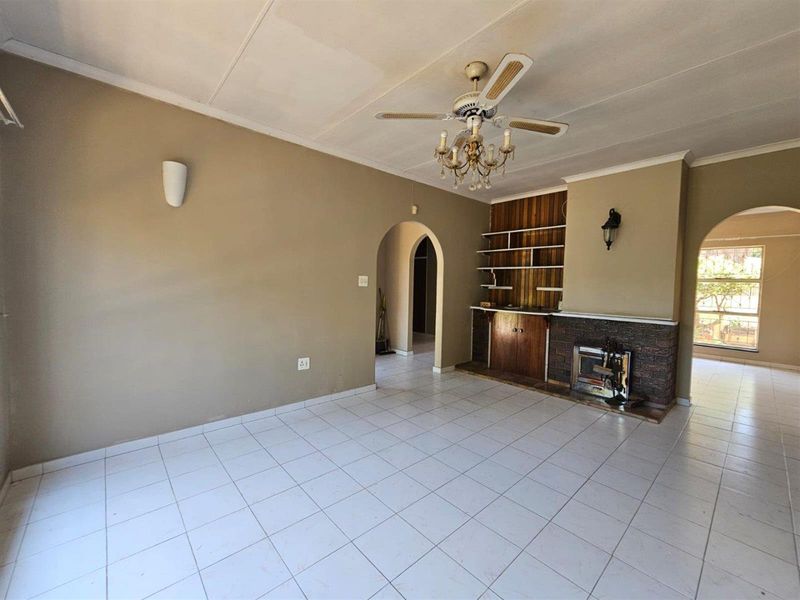 Spacious living room featuring tiled flooring, a built-in fireplace with shelving, and a ceiling fan, offering a blank canvas for renovation.