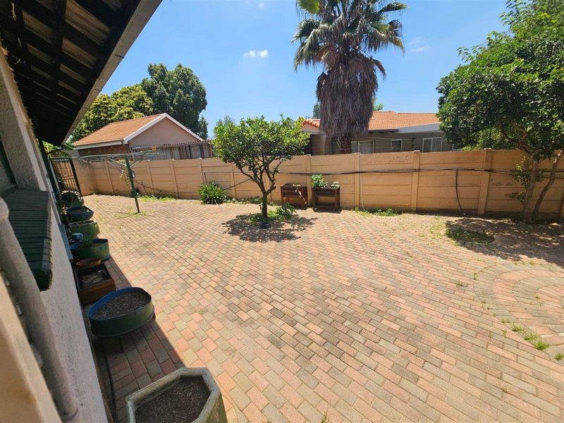 A paved rear courtyard area featuring a precast concrete boundary wall and established garden elements.