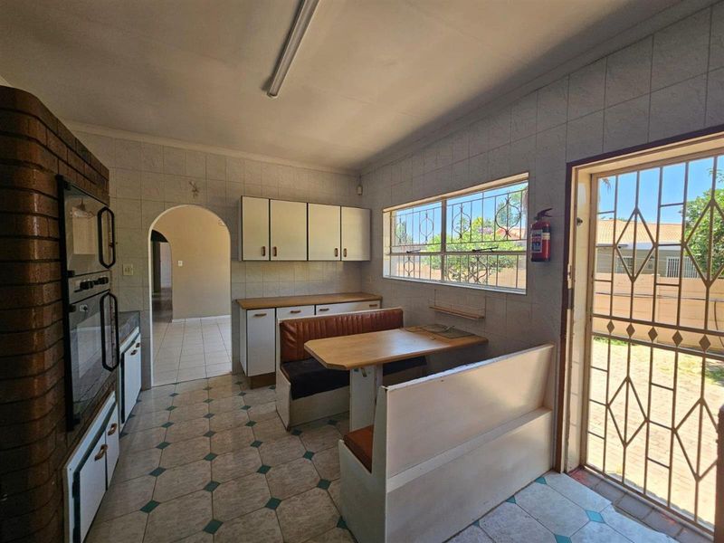 A dated kitchen featuring built-in cabinetry, tiled surfaces, and a built-in oven, with direct access to the exterior through a security gate.