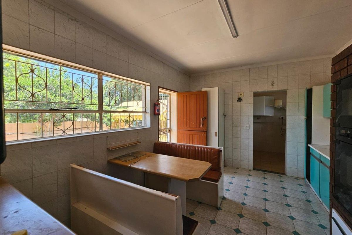 A dated kitchen featuring a built-in breakfast nook, tiled walls and flooring, and direct access to an adjacent utility area.