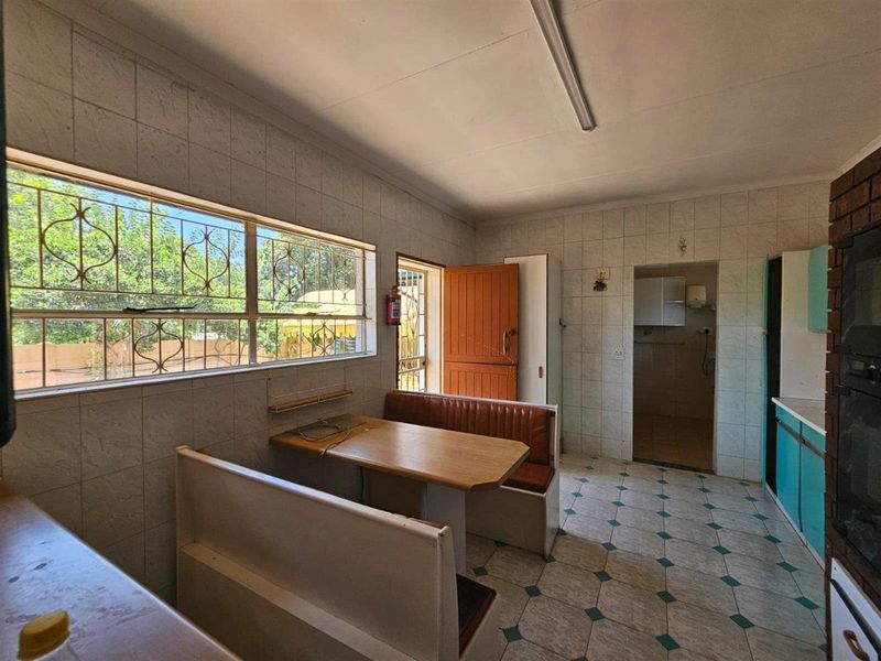 A dated kitchen featuring a built-in breakfast nook, tiled walls and flooring, and direct access to an adjacent utility area.