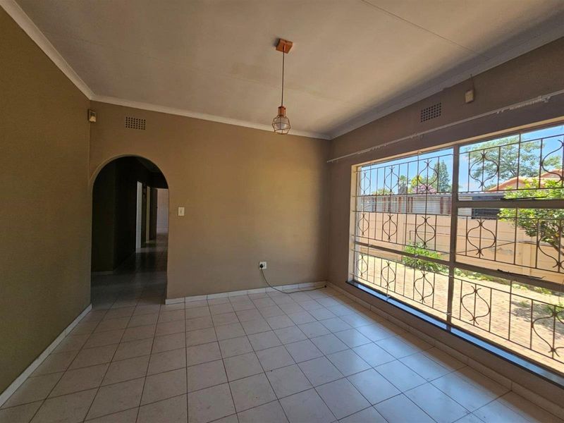 An empty living room featuring tiled flooring, an arched entryway, and large windows fitted with security bars.