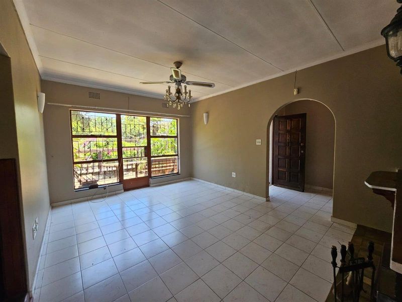 Spacious living room featuring tiled flooring, a ceiling fan, and an arched entryway, offering a blank canvas for renovation and interior design.