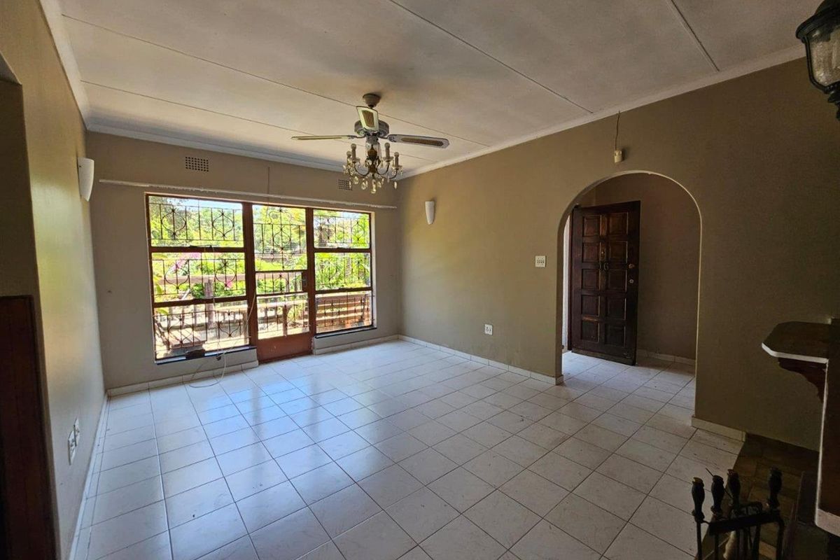 Spacious living room featuring tiled flooring, a ceiling fan, and an arched entryway, offering a blank canvas for renovation and interior design.