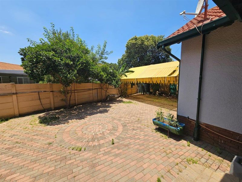 Rear exterior area featuring a paved patio with a circular design, a retractable awning, and perimeter walling.