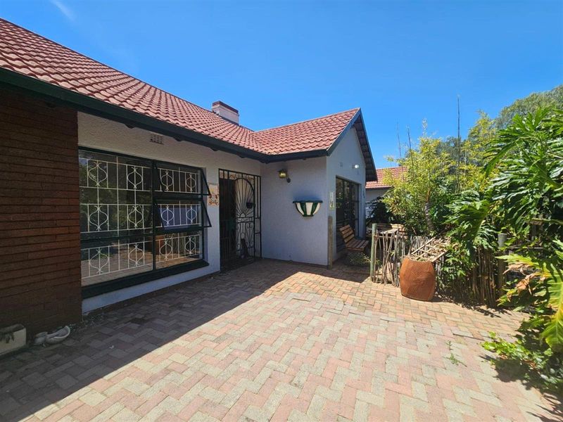 A rear exterior view of the house featuring brick paving, a tiled roof, and secure window grilles.