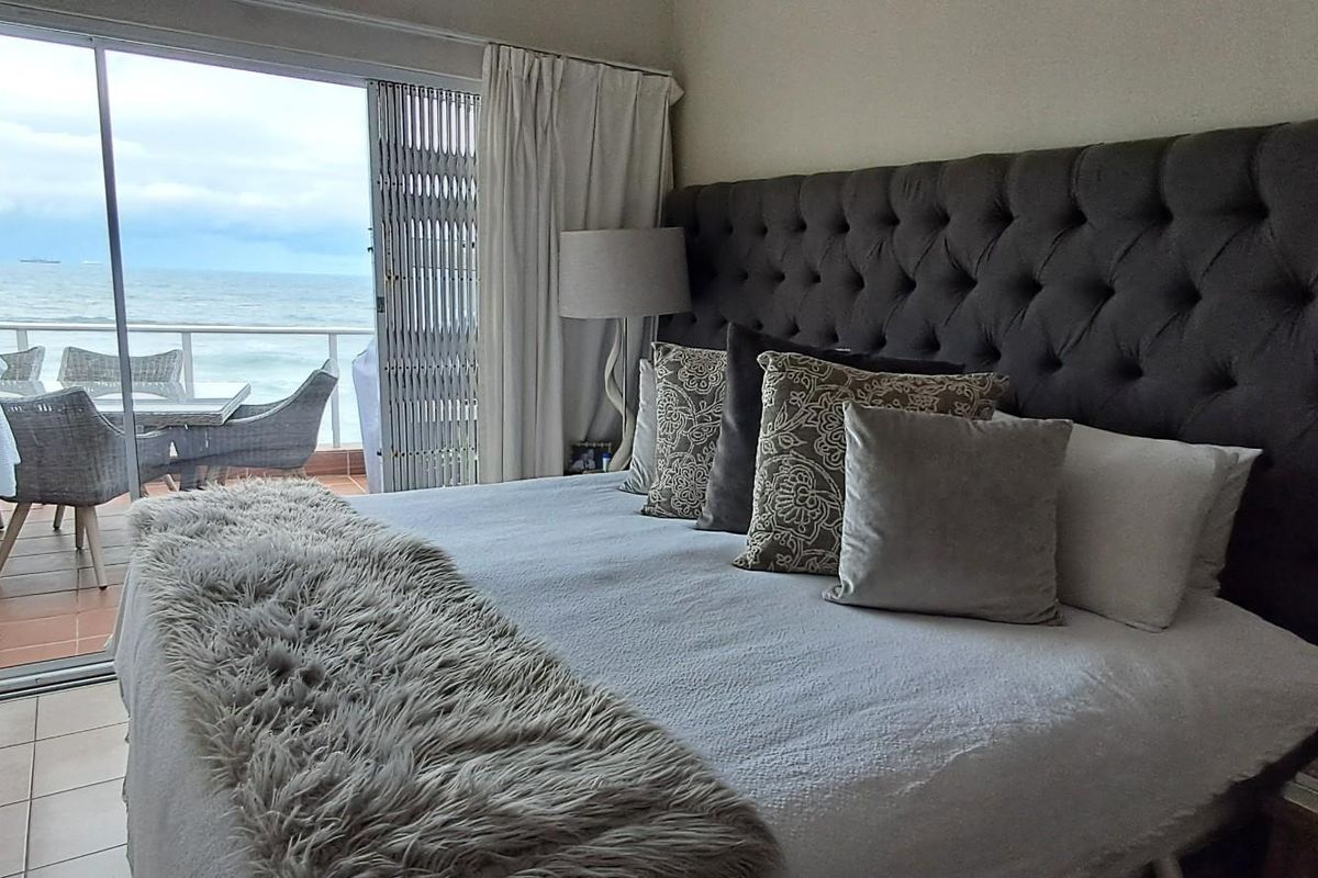 A well-maintained bedroom featuring tiled flooring and large sliding glass doors that open onto a balcony with direct ocean views.