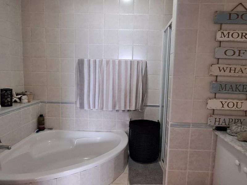 A functional bathroom featuring a corner bathtub, a separate shower enclosure, and a vanity unit with an integrated sink and tiled walls.