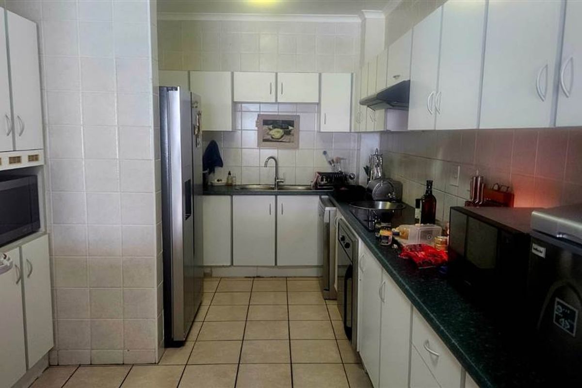 A functional kitchen featuring white cabinetry, dark laminate countertops, tiled splashbacks, and ceramic floor tiles, offering a practical layout for daily meal preparation.