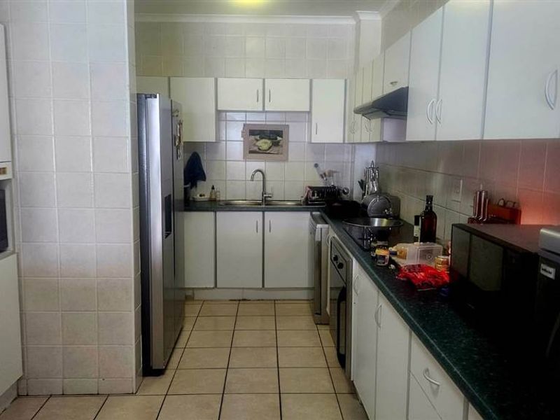 A functional kitchen featuring white cabinetry, dark laminate countertops, tiled splashbacks, and ceramic floor tiles, offering a practical layout for daily meal preparation.