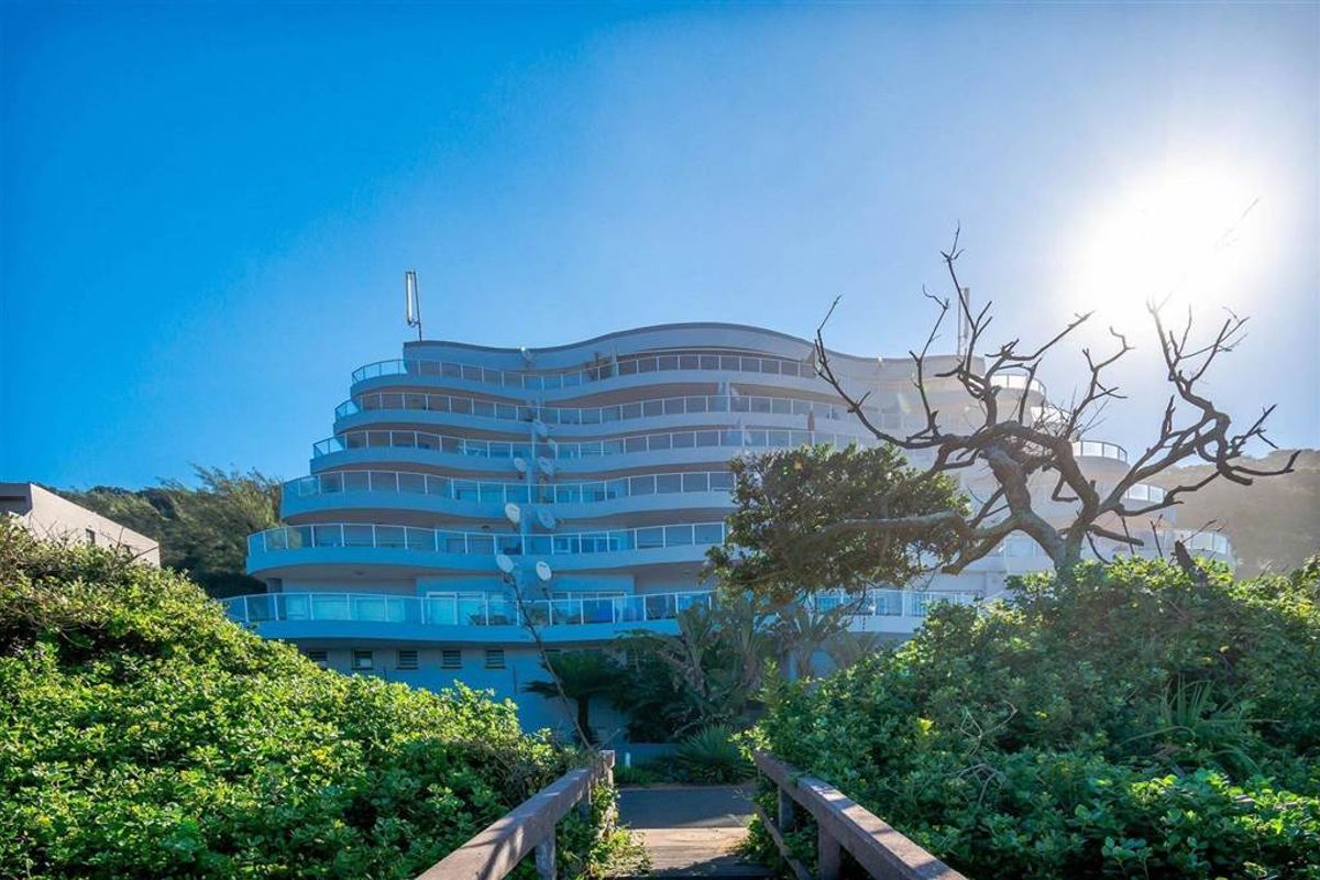 A view of the multi-story apartment building facade featuring tiered balconies with glass balustrades, set against a lush coastal landscape.