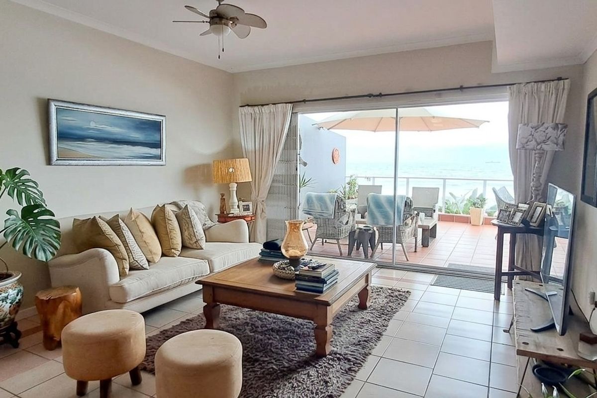A bright living room featuring tiled flooring, a ceiling fan, and large sliding glass doors that open onto a private balcony with ocean views.