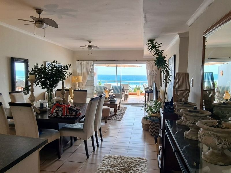 Spacious open-plan living and dining area featuring tiled floors, ceiling fans, and large sliding doors leading to a balcony with ocean views.