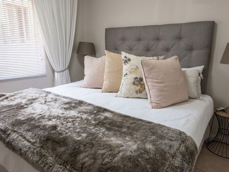 A well-maintained bedroom featuring neutral wall tones, tiled flooring, and a window fitted with venetian blinds.