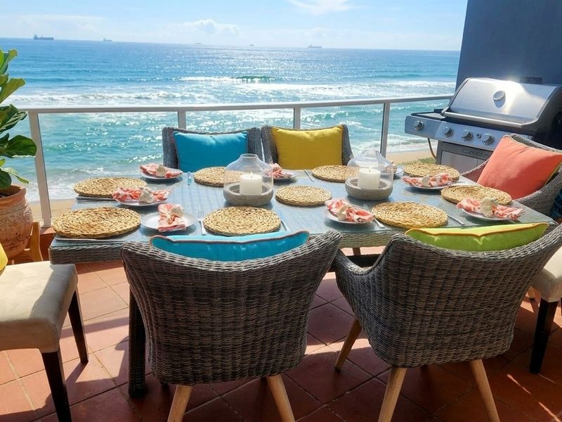 A spacious balcony featuring tiled flooring, a glass balustrade, and a built-in gas grill, offering stunning direct ocean views.