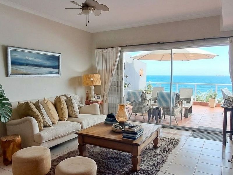 A bright living room featuring tiled floors and a ceiling fan, with large sliding glass doors opening onto a balcony with ocean views.