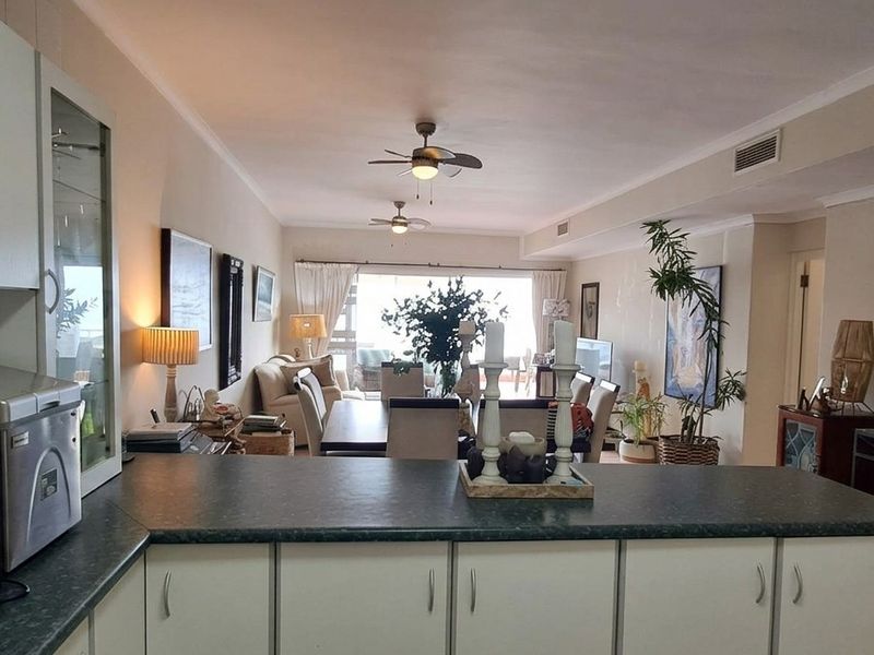 An open-plan living and kitchen area featuring functional cabinetry, laminate countertops, and ceiling fans, leading out to a balcony through sliding glass doors.