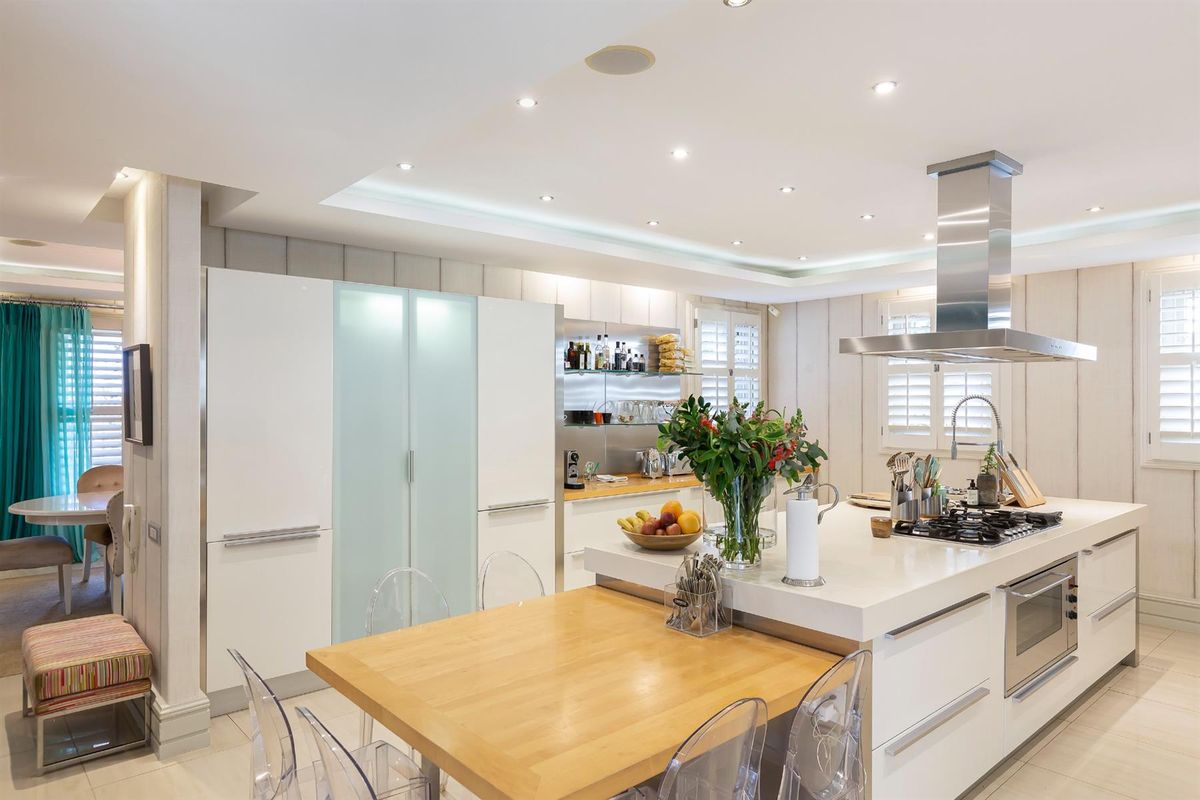 Modern kitchen featuring a large central island with integrated gas hob, stainless steel extractor fan, built-in oven, and sleek white cabinetry.