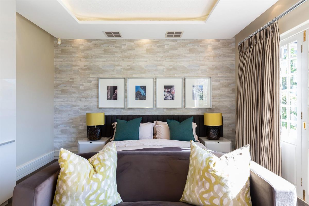 A well-appointed bedroom featuring a textured feature wall, recessed ceiling lighting, and direct access to an outdoor area through a glass-paned door.