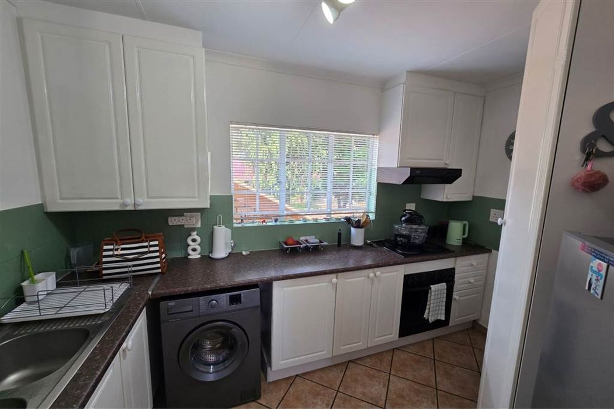 A functional kitchen featuring white cabinetry, dark laminate countertops, tiled splashbacks, and integrated appliances including an oven and extractor fan.