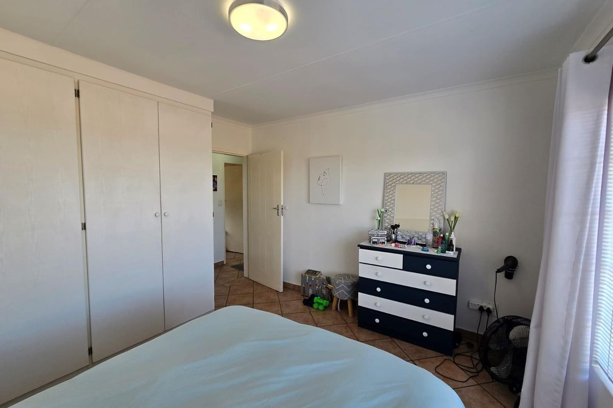 A bedroom featuring built-in cupboards, tiled flooring, and a ceiling light fixture, offering a functional and neutral living space.