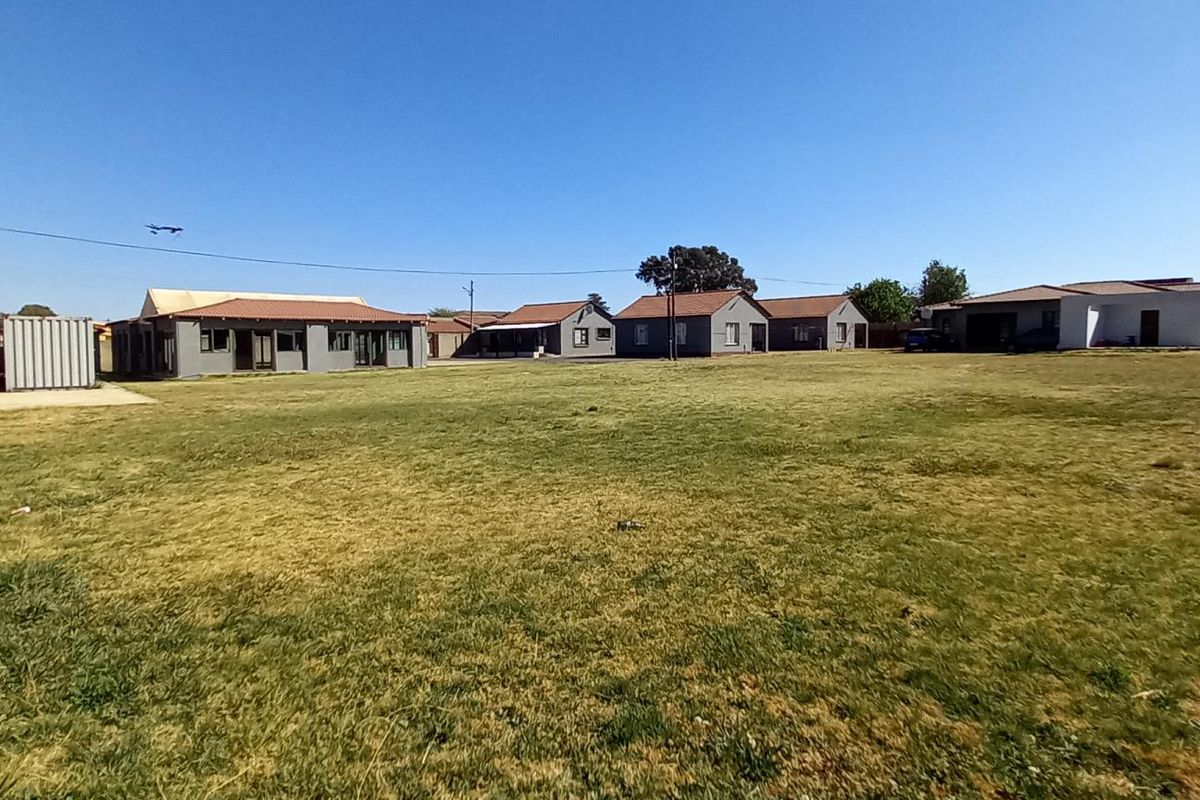 A wide-angle view of the guest house property grounds, featuring multiple detached building structures set within a large, open grassed area.