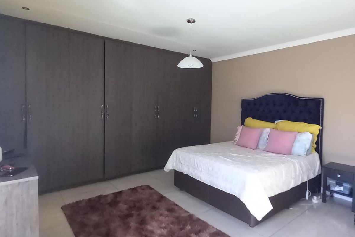A spacious bedroom featuring extensive floor-to-ceiling built-in dark wood cabinetry, tiled flooring, and recessed ceiling lighting.