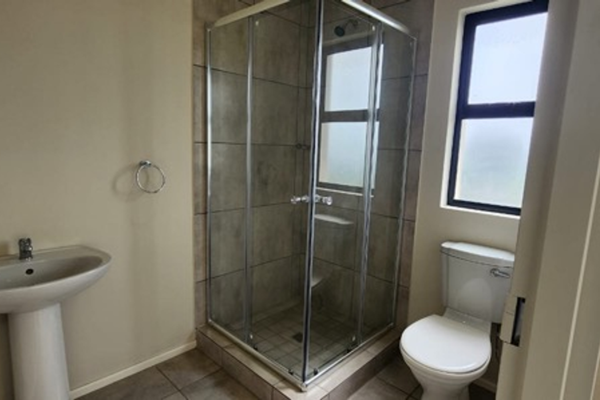 A functional bathroom featuring a corner shower enclosure, pedestal basin, and toilet with neutral tiled flooring and shower wall finishes.
