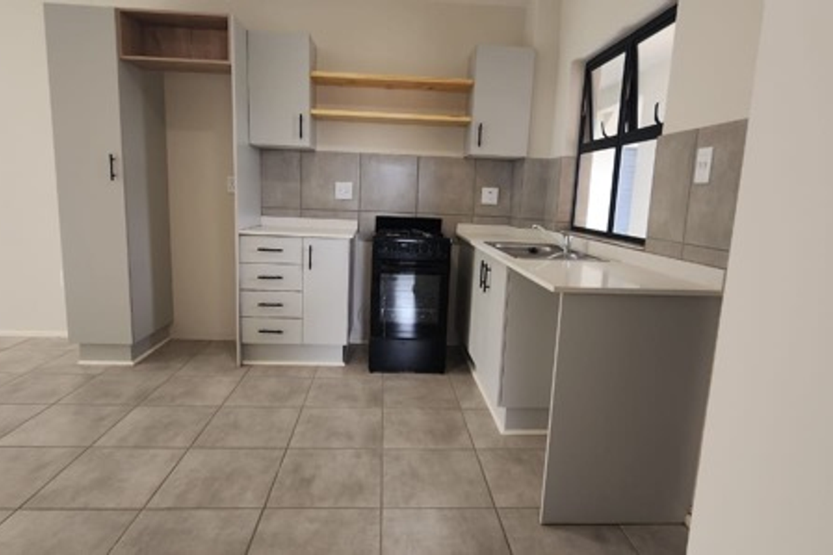 A modern, clean kitchen featuring light grey cabinetry, stone countertops, a tiled backsplash, and a freestanding stove, presented in an empty, well-maintained space.
