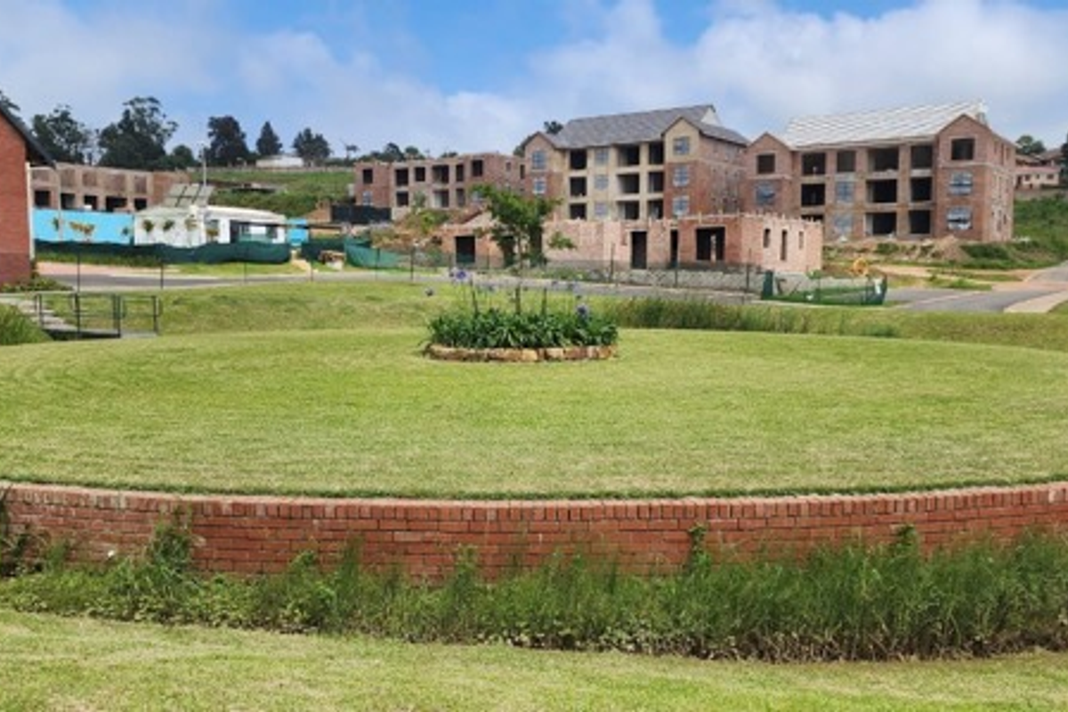 A view of a landscaped circular garden area with a brick retaining wall, set within a developing residential townhouse estate.