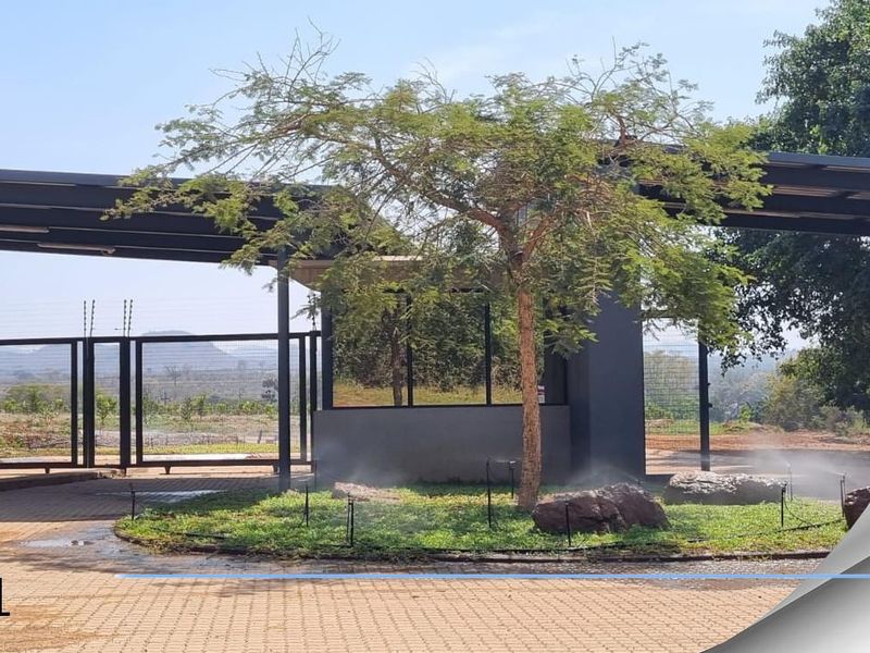 Entrance gate and security guardhouse for the residential estate, featuring paved driveway, modern metal structure, and landscaped island with irrigation.