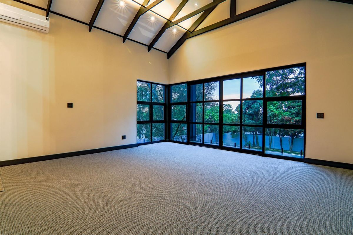 Spacious living area featuring high vaulted ceilings with exposed beams, large floor-to-ceiling windows, and wall-mounted air conditioning unit.