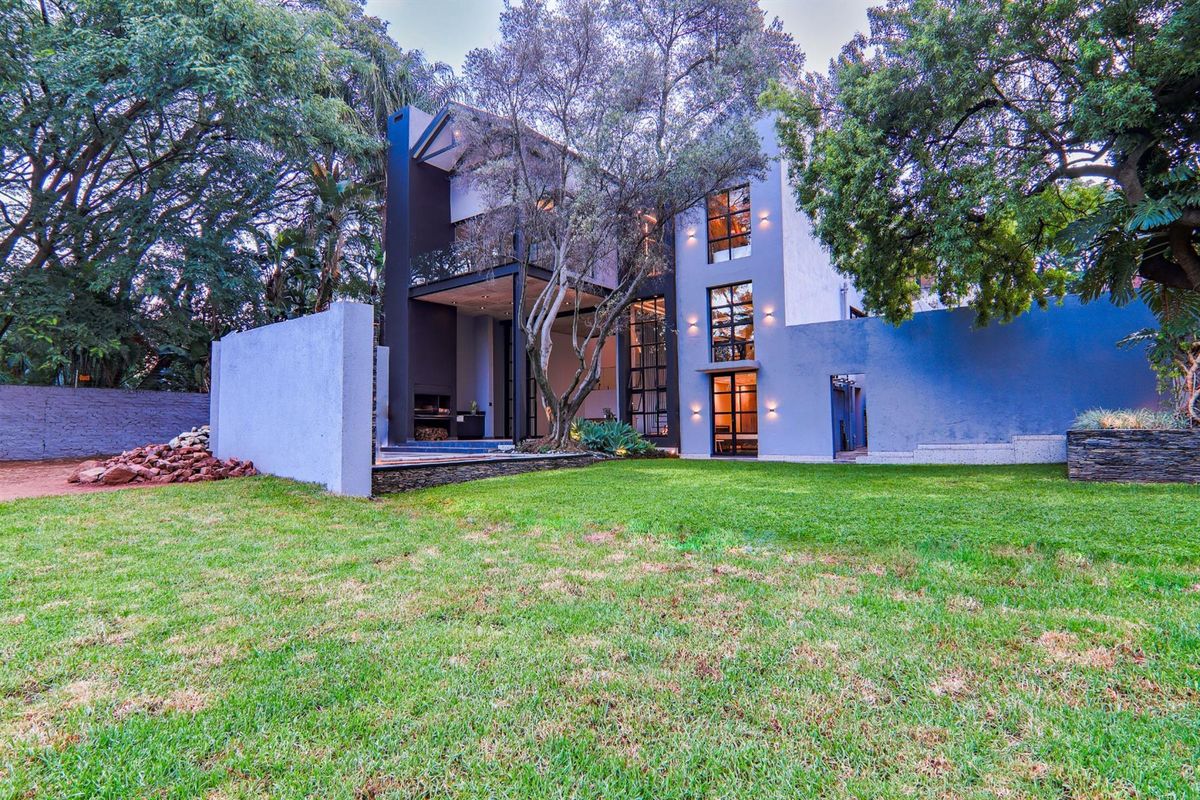 A modern multi-story residence featuring a contemporary facade, large glass windows, and a spacious landscaped rear garden with mature trees.
