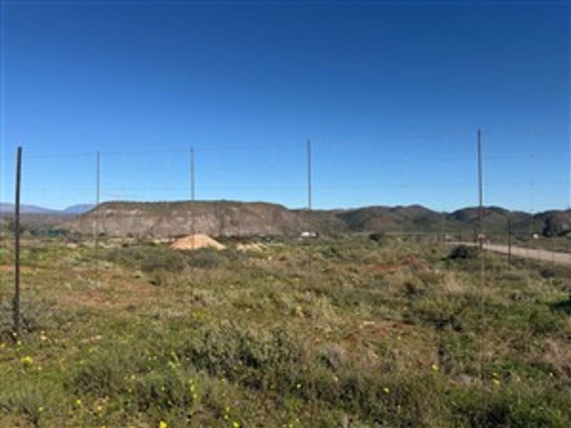A vacant residential plot featuring natural vegetation, wire fencing, and scenic mountain views in the background.