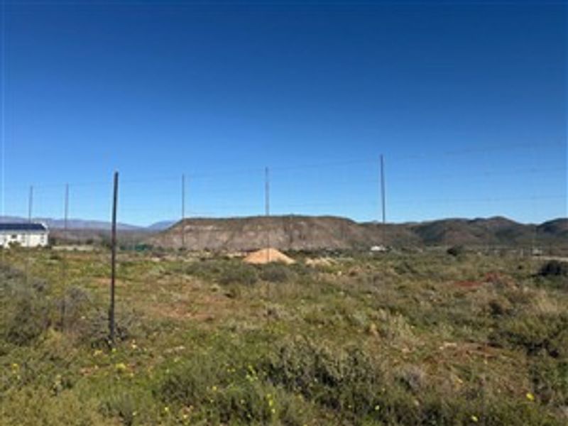 A vacant residential plot featuring natural scrub vegetation, wire perimeter fencing, and scenic mountain views in the background.