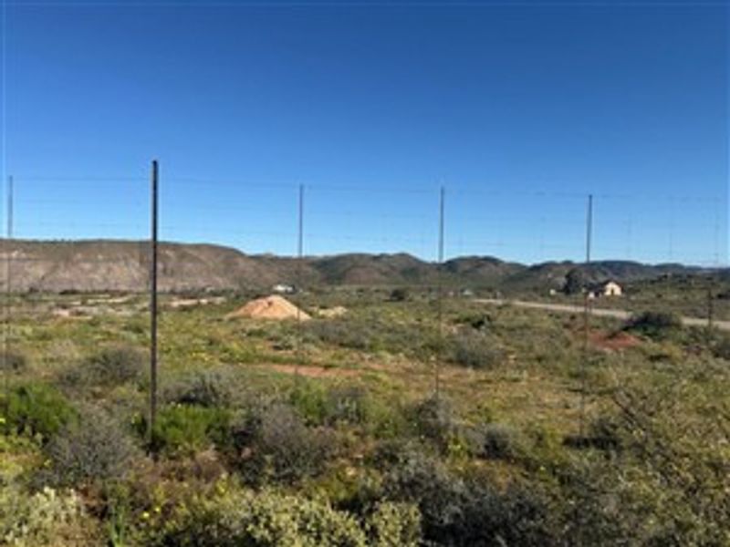 A view of a vacant residential plot featuring natural landscape, wire fencing, and distant mountain views.