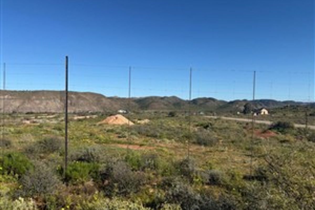 A view of a vacant residential plot featuring natural landscape, wire fencing, and distant mountain views.