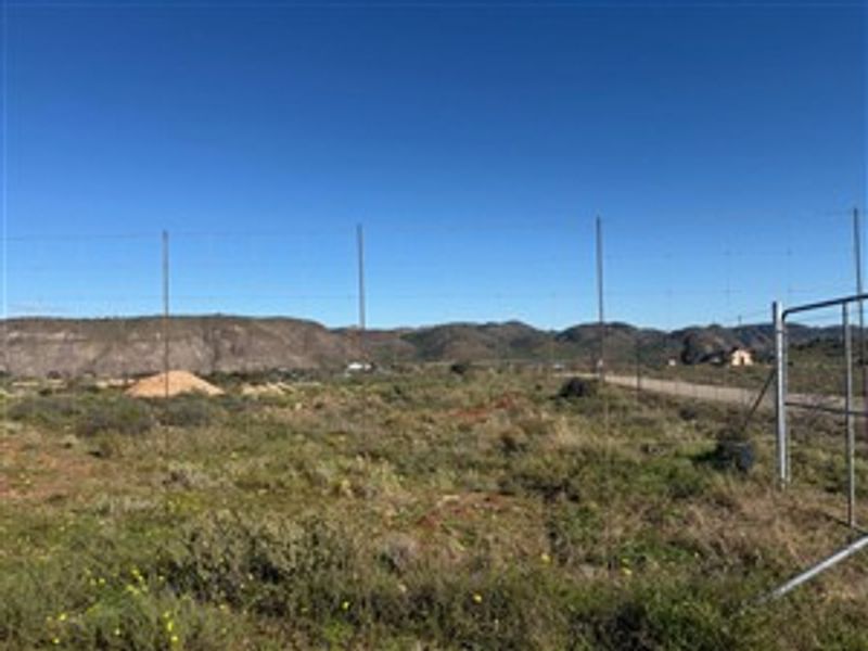 A vacant residential plot featuring wire fencing and a metal gate, set against a scenic mountainous landscape.