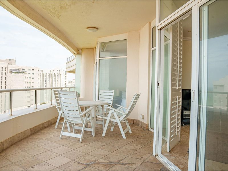 A spacious covered balcony featuring tiled flooring, a metal balustrade, and direct access to the interior through large sliding glass doors.