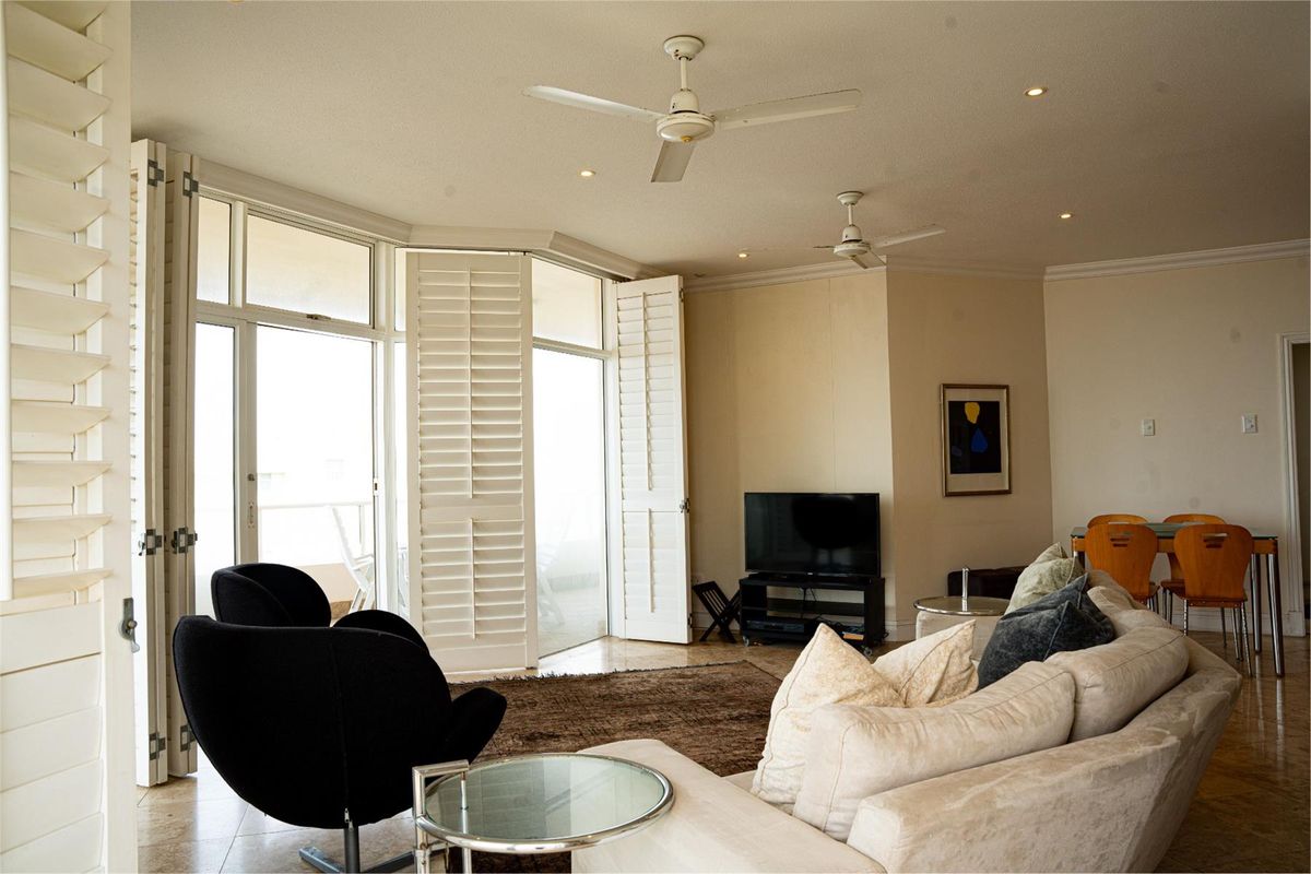 Spacious living room featuring tiled flooring, recessed lighting, ceiling fans, and large plantation shutters opening to a balcony area.