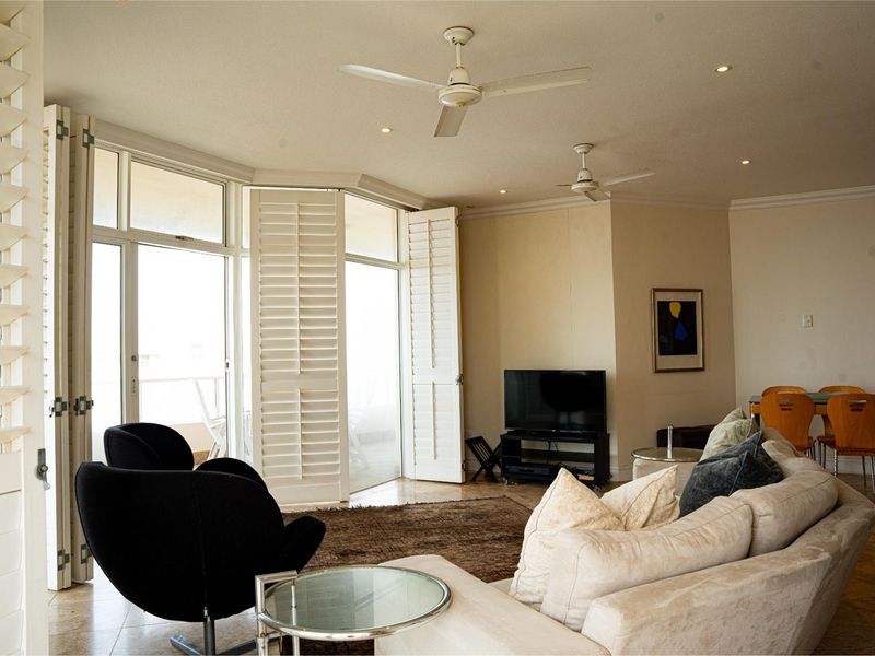 Spacious living room featuring tiled flooring, recessed lighting, ceiling fans, and large plantation shutters opening to a balcony area.