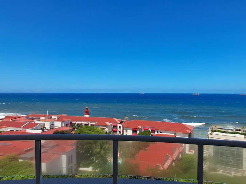 Panoramic ocean view from a high-rise apartment balcony featuring a modern glass balustrade overlooking the coastline and surrounding buildings.