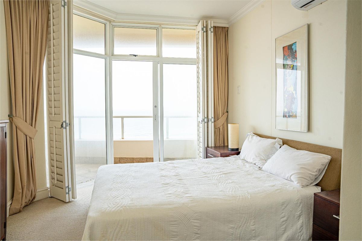 A bright bedroom featuring carpeted flooring, plantation shutters, and direct access to a private balcony through sliding glass doors.