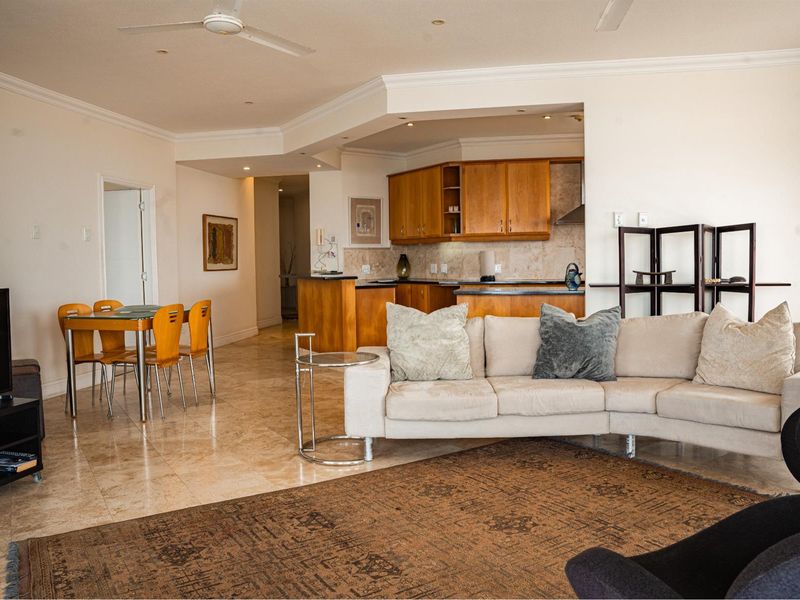 Open-plan living and dining area featuring stone flooring, recessed lighting, and a functional kitchen with wooden cabinetry and stone countertops.