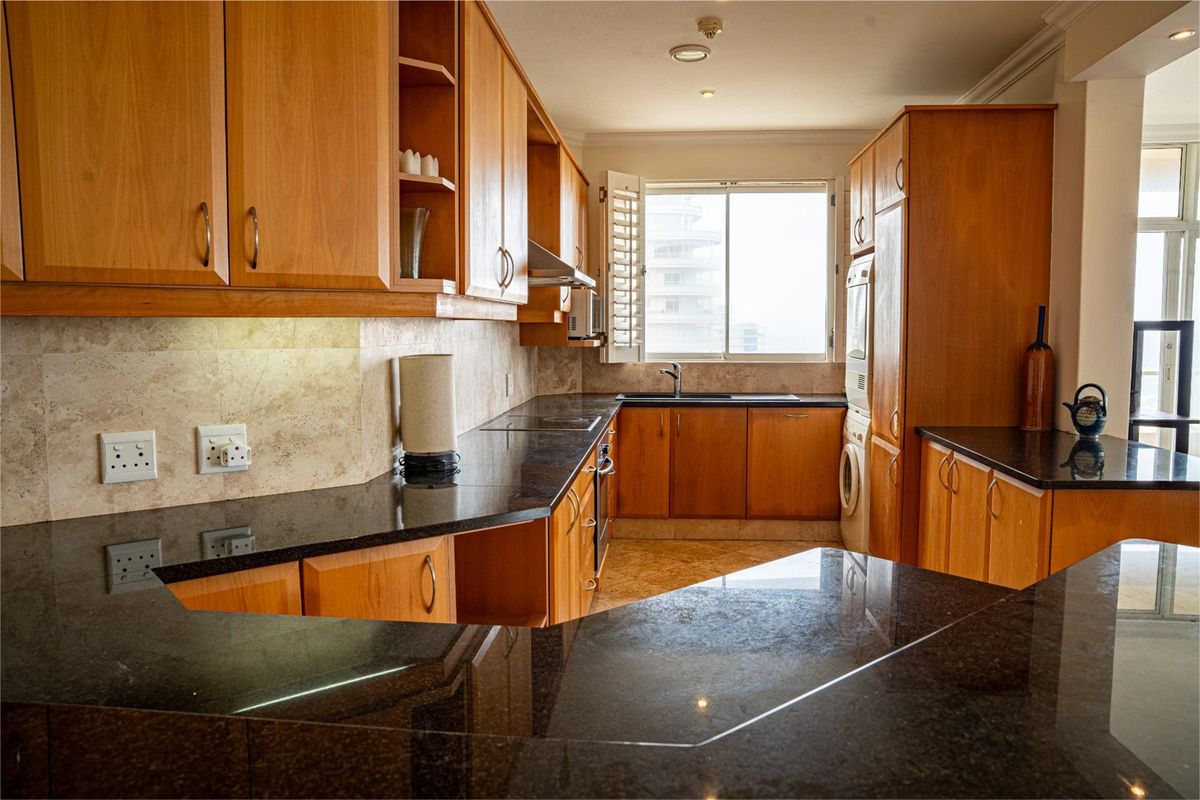 A functional kitchen featuring warm wooden cabinetry, dark granite countertops, integrated appliances, and a tiled backsplash with ample storage space.