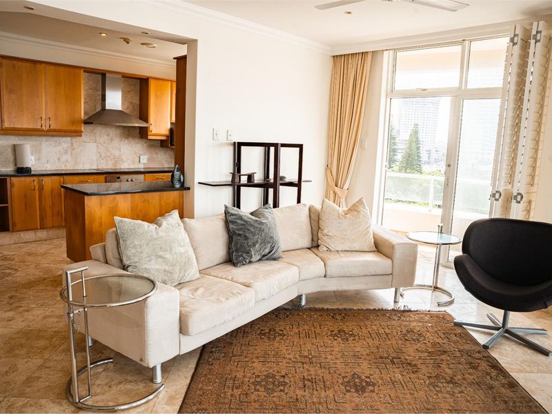 Open-plan living area featuring stone tile flooring, a functional kitchen with wooden cabinetry and granite countertops, and direct access to a balcony.