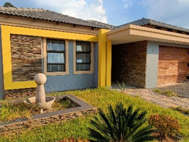 Modern front elevation featuring stone cladding, yellow accent walls, a double garage, and a landscaped front garden with a water feature.