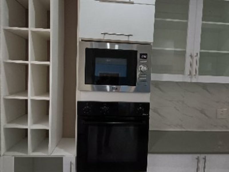 Modern kitchen featuring built-in oven and microwave, glass-fronted cabinetry, wine storage, and stone-look backsplash with quartz countertops.