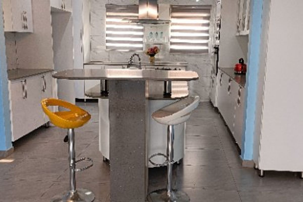 A functional kitchen featuring white cabinetry, a central island with seating, tiled flooring, and modern roller blinds.